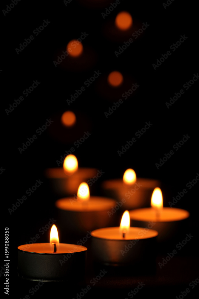 Many candle flames glowing in the dark.