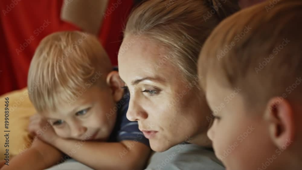 Closeup of joyous mother lying on floor with two little sons, smiling, talking and watching something on digital tablet Closeup of joyous mother lying on floor with two little sons, smiling, talking and watching something on digital tablet