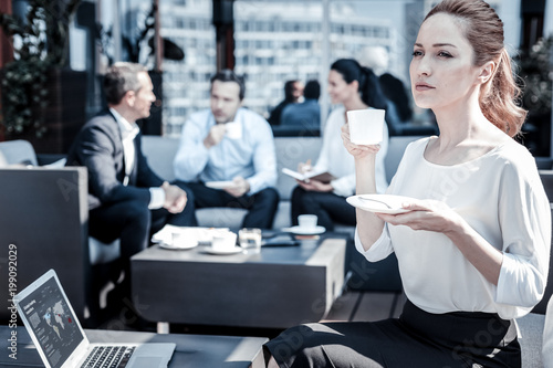 Business women. Smart confident nice woman sitting in front of the laptop and having coffee while taking a break from work