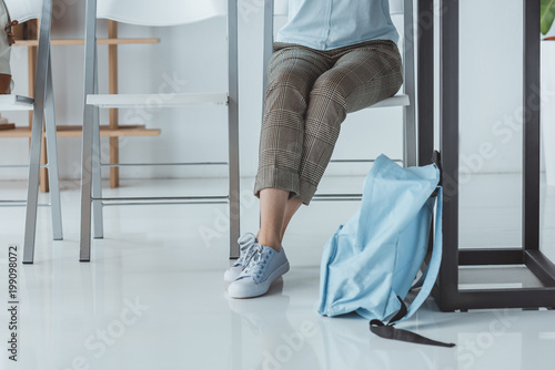 low section view of girl sitting at table with backpack on floor