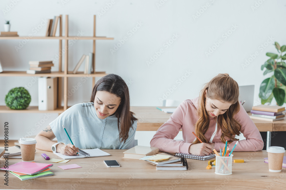 female multiethnic students writing examination together female multiethnic students writing examination together