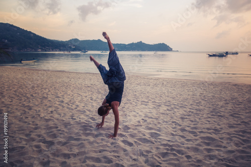 a girl stands on her hands on a sandy beach, enjoys life with freedom and youth