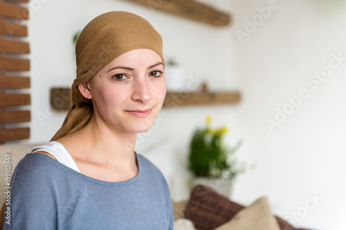 Fotografie Portrait of young positive adult female cancer patient sitting in living room, smiling and looking at the camera