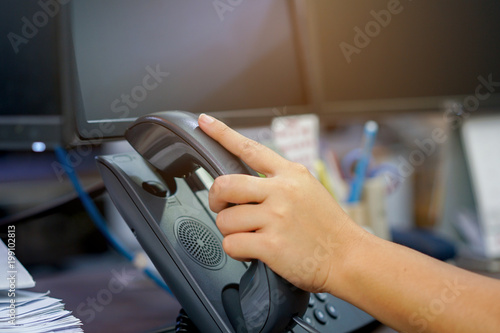 close up woman hand touching handset on telephone for receiving call from customer at office desk photo