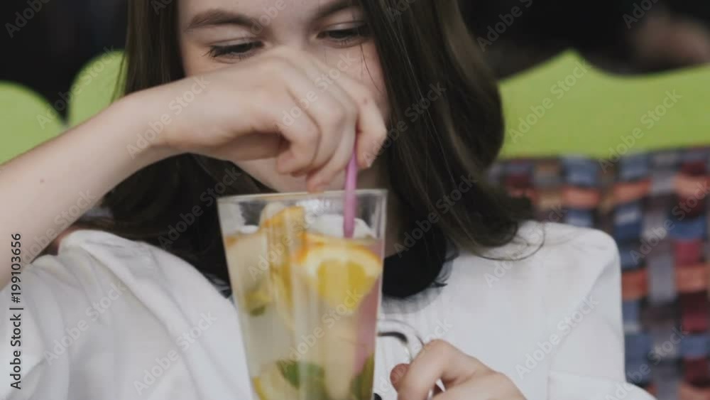 Beautiful girl stirring lemonade with tubule and smiling at camera Beautiful girl stirring lemonade with tubule and smiling at camera
