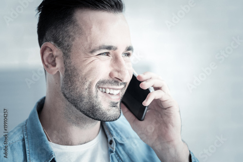 Distance communication. Portrait of a happy cheerful nice man smiling and putting a phone to the ear while making a call