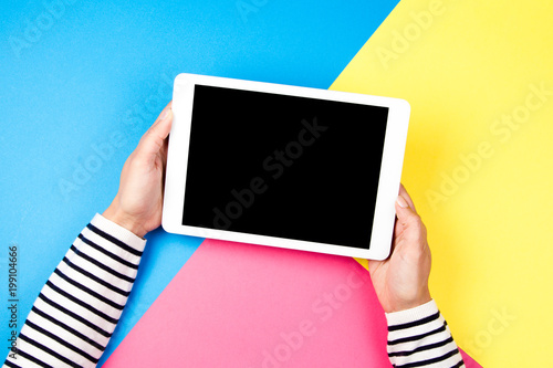 Woman's hands with tablet computer on colorful background.