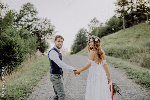Beautiful bride and groom in green nature, holding hands.