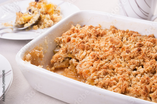 Freshly baked apple crumble in a baking dish and a portion on a plate. Selective focus