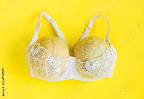 Breast enlargement concept, white bra with two melons on yellow background