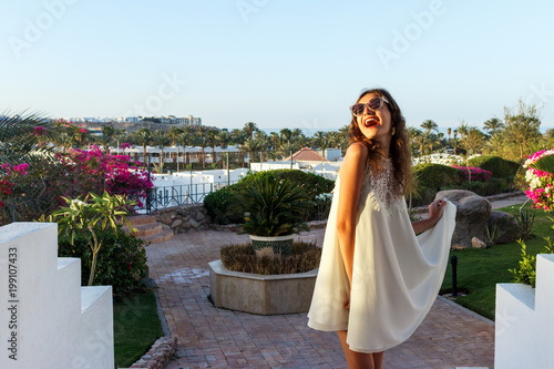 beautiful girl in white dress and Sunglasses. Happy woman smiling and looking at the sun. Sunny summer day under the sun in the park