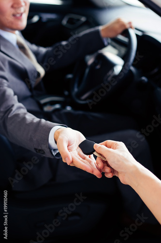 Smiling and happy man receiving a car key from car dealer salesman - car rental and sales concept.