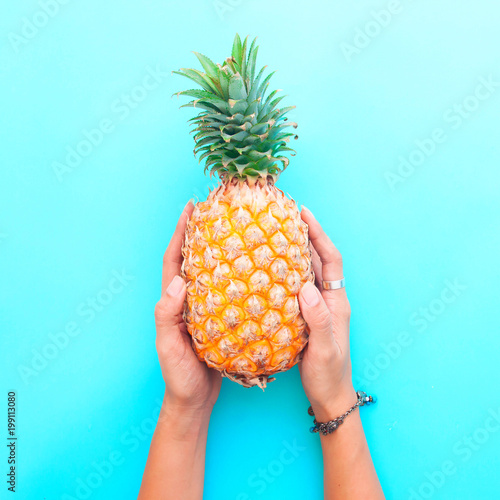 Woman's hands holding pineapple on blue color background, Summer holiday concept
