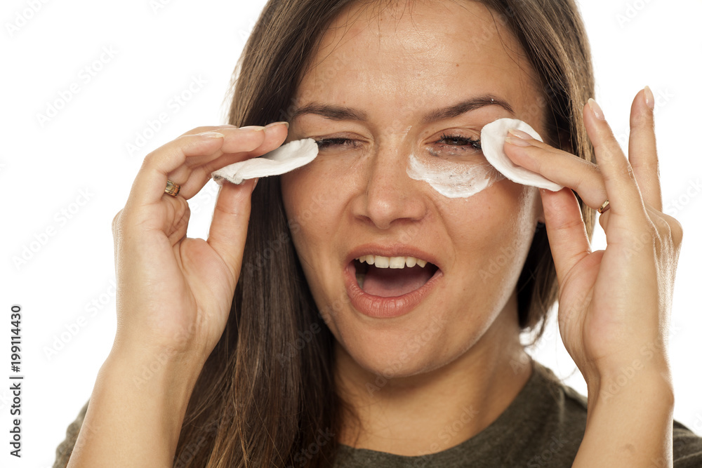 Young beautiful woman celaning her face with cotton pads on white background Young beautiful woman celaning her face with cotton pads on white background
