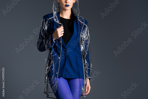 Woman posing in blue jacket and transparent raincoat isolated on dark background