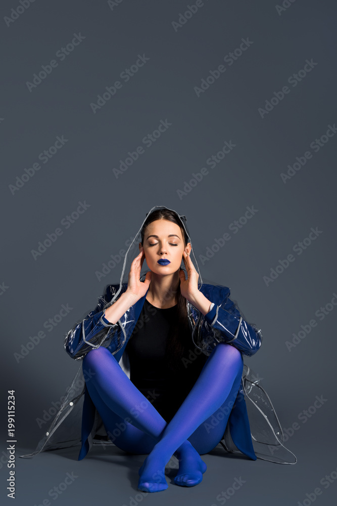 Obraz premium Girl wearing transparent raincoat and blue pantyhose sitting on dark background