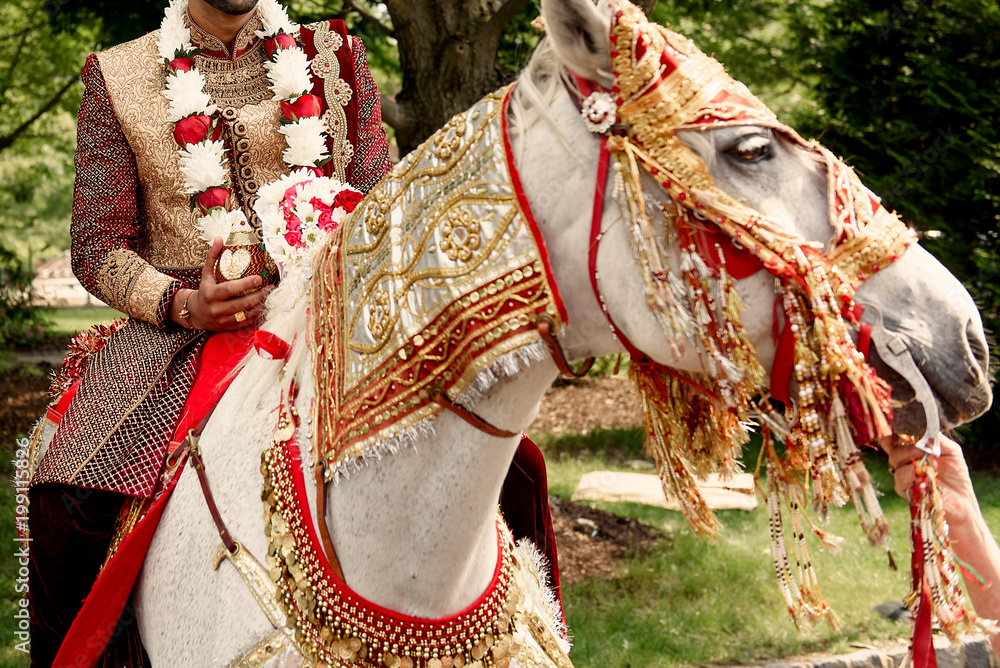 Smiling Indian groom in red suit rides a white horse