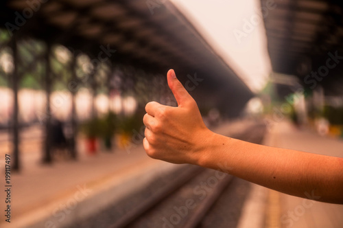 hand of human showing thumb up with blurred straight railway back ground at station.