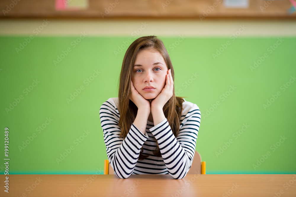 Sad student sitting in classroom with her head in hands. Education, high school, bullying, pressure, depression and teenagers concept. Sad student sitting in classroom with her head in hands. Education, high school, bullying, pressure, depression and teenagers concept.