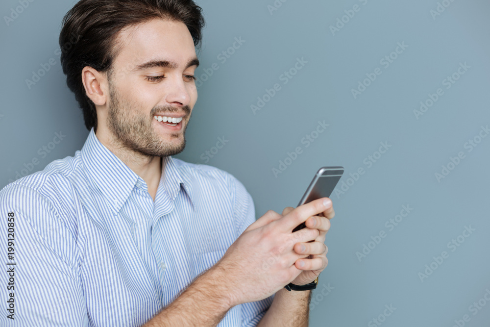 Online communication. Happy nice positive man looking at the screen and smiling while talking with his friends online Online communication. Happy nice positive man looking at the screen and smiling while talking with his friends online