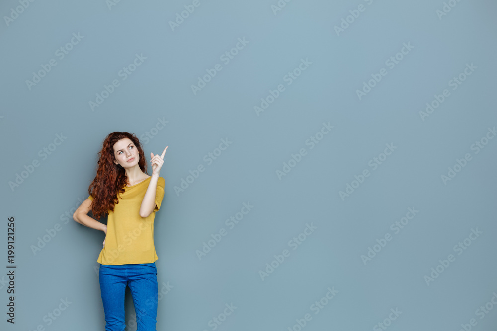 Look there. Smart nice delighted woman standing against background and pointing with her finger while being in a great mood Look there. Smart nice delighted woman standing against background and pointing with her finger while being in a great mood