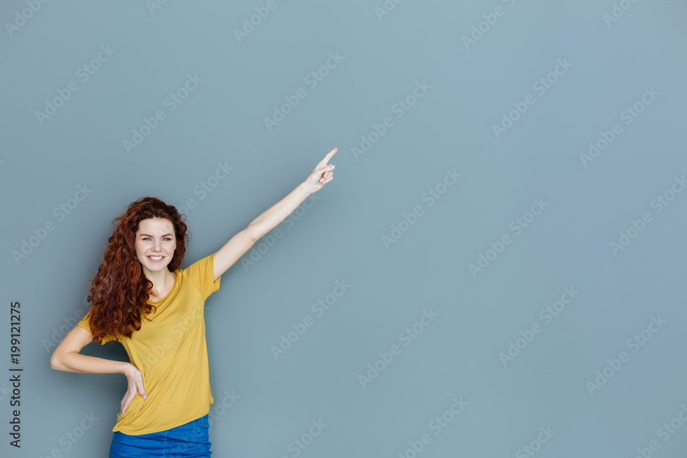 This direction. Happy delighted nice woman smiling and pointing with her hand while looking at you This direction. Happy delighted nice woman smiling and pointing with her hand while looking at you