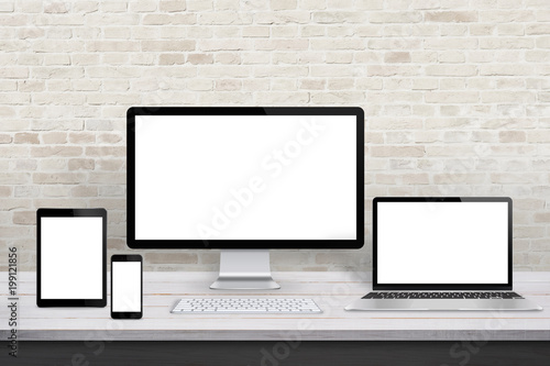 Multiple display devices for responsive web desing promotion. Modern office desk with brick wall in background.