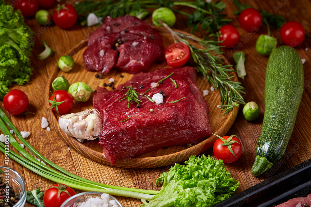 Still life of raw beef meat with vegetables on wooden plate over vintage background, top view, selective focus