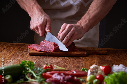 Strong professional man's hands cutting raw beefsteak, selective focus, close-up