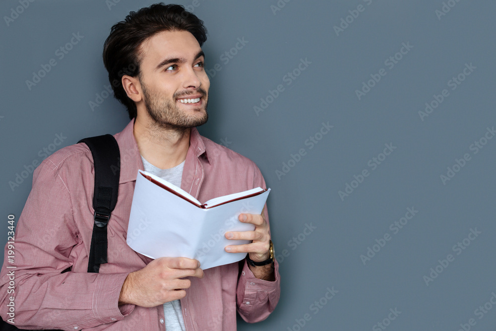 Young tourist. Nice positive handsome man reading a tour guide and smiling while planning his next trip Young tourist. Nice positive handsome man reading a tour guide and smiling while planning his next trip