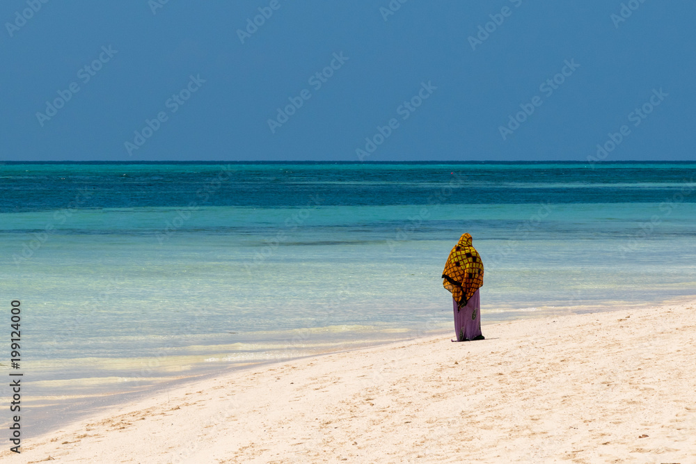 a traditional Muslim African woman walks along the coast of the ocean