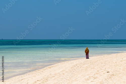 a traditional Muslim African woman walks along the coast of the ocean