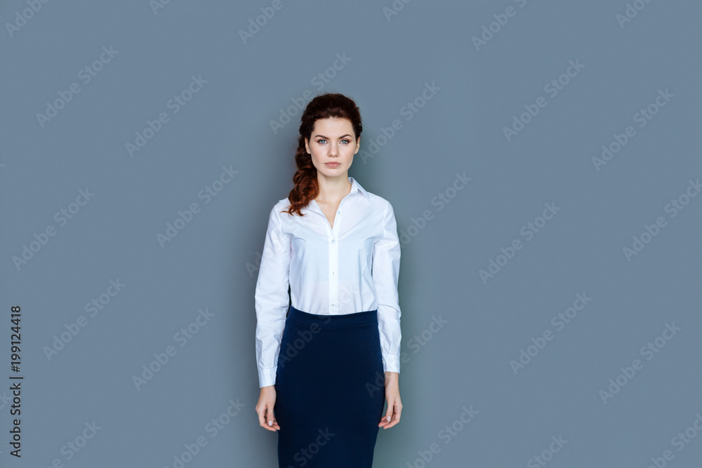 Professional success. Smart nice confident businesswoman standing against grey background and looking at you while working Professional success. Smart nice confident businesswoman standing against grey background and looking at you while working