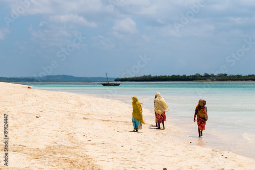 Тraditional African Muslim girls on walking along the beach of the ocean.Zanzibar