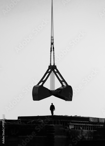 Black silhouette of the figure of a man under the bucket of a port crane © Vyacheslav