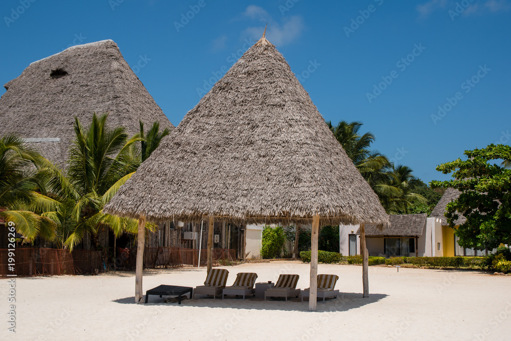 Bamboo hut with Beach bed among palm trees at perfect tropical coast fresh green palm trees around standing at the white sand beach and cloudless blue sky on a sunny day. Spa concept.