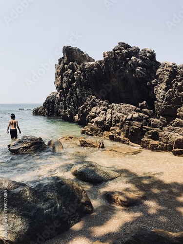 the child is standing in the sea next to the rocks. thailand malaysia