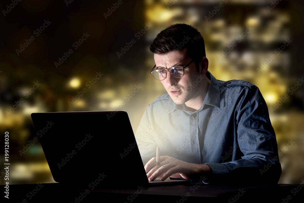 Young handsome businessman working late at night in the office with city lights in the background