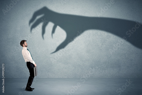 Fotografie Business person afraid of a big monster claw shadow concept on background