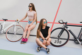 Cycling and fitness. Young beautiful fit women with perfect bodies in sportswear near the bikes outdoors on the track. Sportive and healthy lifestyle, cyclist working out, training, fashion, beauty.