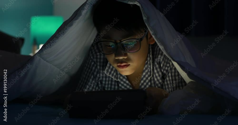 Young boy playing with a cellphone or smartphone on a bed. night Young boy playing with a cellphone or smartphone on a bed. night