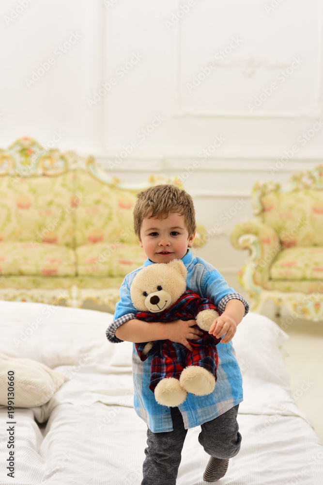 Boy with happy face holds favourite toy fluffy bear. Child with soft teddy bear in hands. Kid play with plush bear, luxury interior background. Happy childhood concept. Little cute toddler carries toy Boy with happy face holds favourite toy fluffy bear. Child with soft teddy bear in hands. Kid play with plush bear, luxury interior background. Happy childhood concept. Little cute toddler carries toy