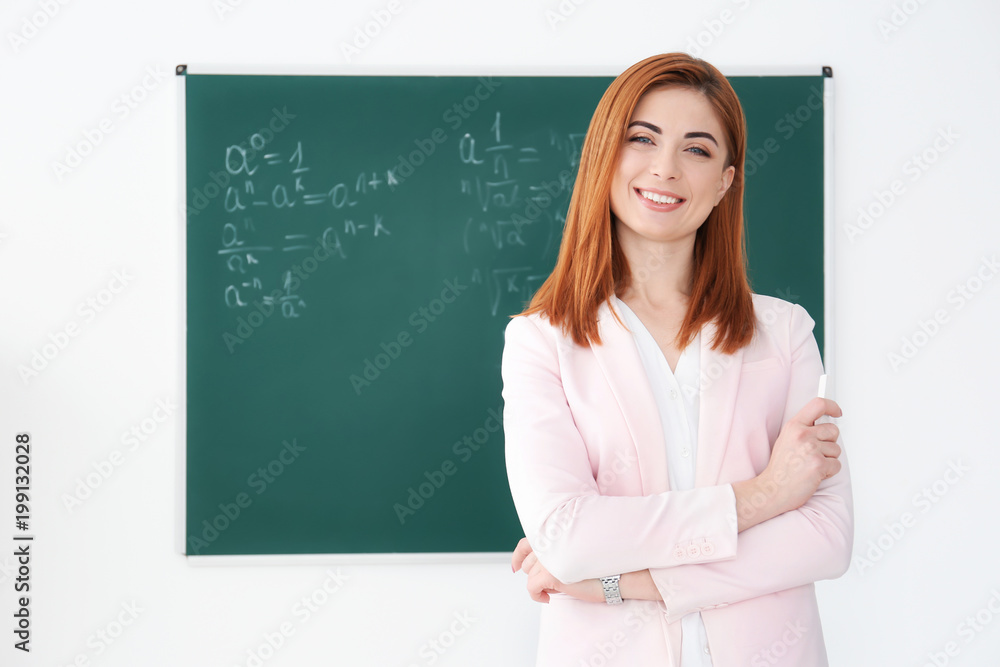 Beautiful young teacher near blackboard in classroom