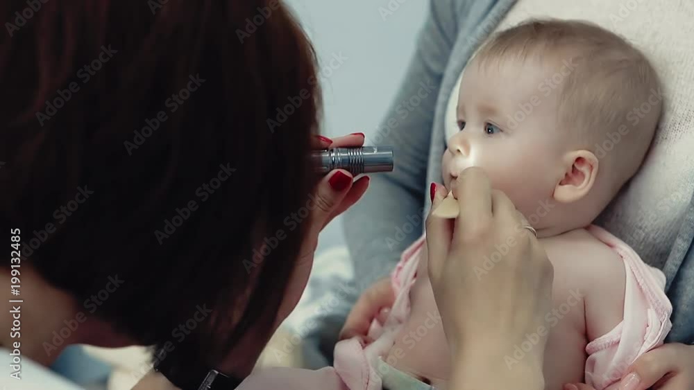 Young beautiful mother is holding a baby on her lap. The doctor examines the child's throat Young beautiful mother is holding a baby on her lap. The doctor examines the child's throat