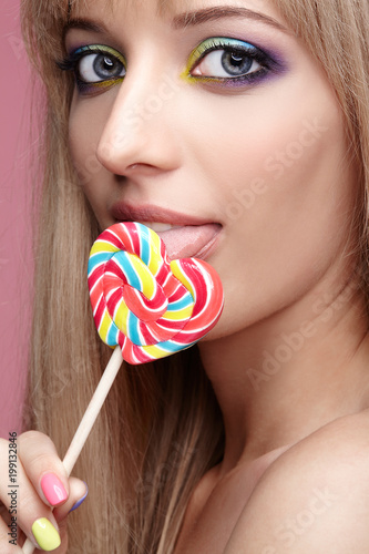 Beauty portrait of young blonde woman on pink background. Female with candy lollipop on stick in hands. photo