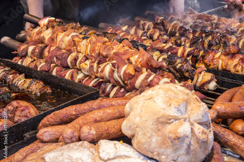 A lot of different meats and sausages are on the counter and grilled, during the street festival