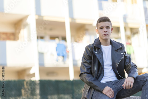 Stylish young man in leather jacket looking at camera, sitting in a park