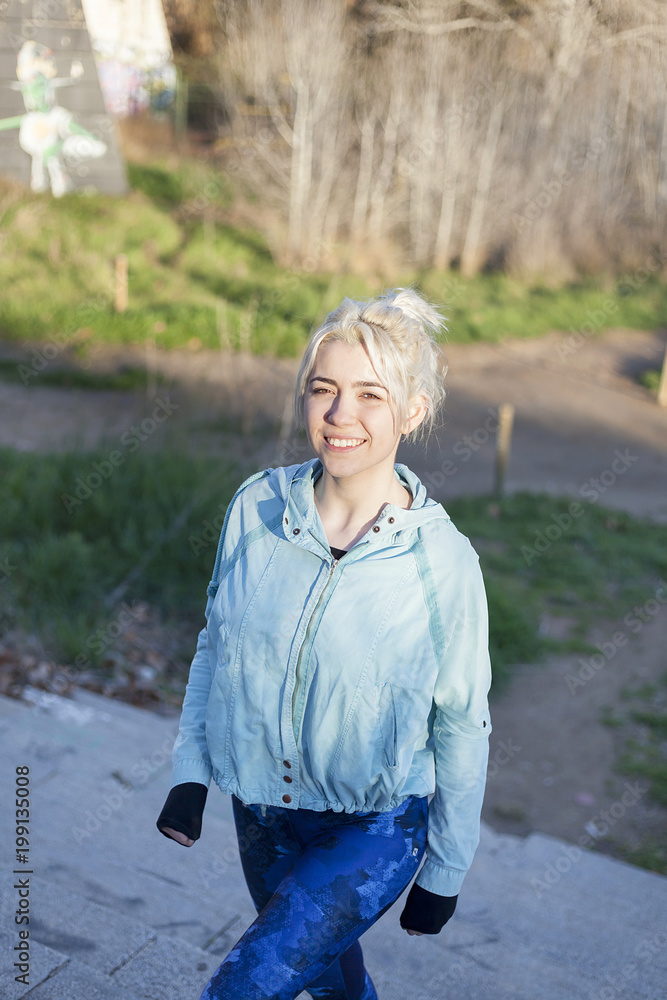 Fototapeta premium Active cheerful blonde pausing after a run in a park on a sunny day