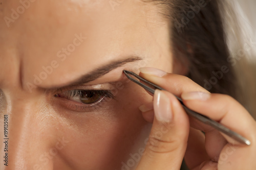 Young beautiful woman pluck her eyebrows with tweezers