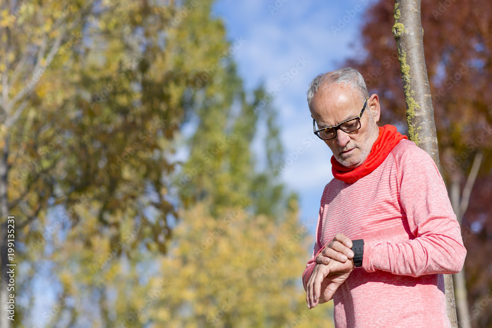 Senior runner man resting at the park while monitoring his exercise Senior runner man resting at the park while monitoring his exercise